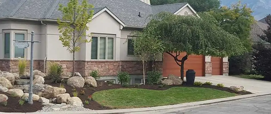 New landscape design including plants, trees, shrubs, flowers, and boulders in front of a home in Draper, UT.
